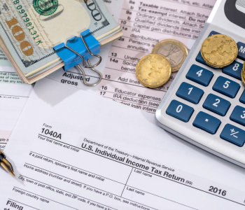 US-Steuerformular mit Kugelschreiber, Taschenrechner und Kleingeld sowie Geldscheinbündel.