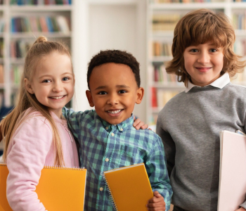 Drei Kinder posieren mit Notizbüchern und lächeln in die Kamera