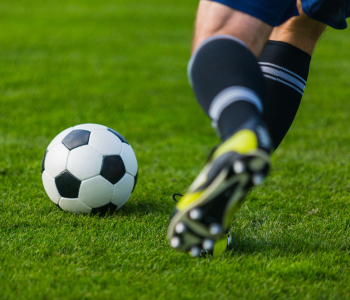 Fußballer-Beine wollen einen Fußball auf grünem Rasen kicken. 
