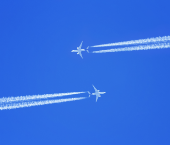 Zwei Flugzeuge fliegen am strahlend blauen Himmel und hinterlassen Kondensstreifen. 