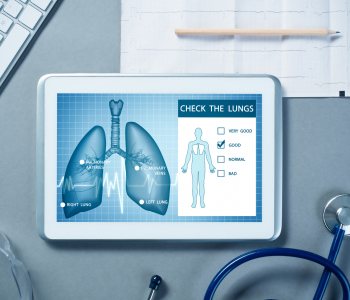 Tablet mit Lungengrafik liegt auf Schreibtisch mit Stethoskop, Tastatur, Brille und Bleistift auf Papier.