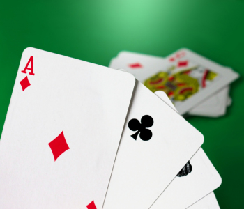 Kartenspiel mit vier Assen auf der Hand im Vordergrund, abgelegte Karten auf einem Stapel im Hintergrund auf einem grünen Tischtuch.