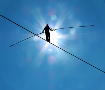 Mann balanciert auf einem Hochseil mit einem Balance-Stab gegen die Sonne bei klarem Himmel.