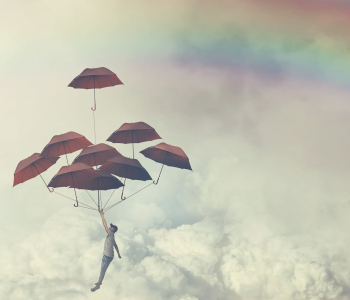 Ein Geschäftsmann hängt an vielen Regenschirmen in einem wolkenverhangenen Himmel mit Regenbogen