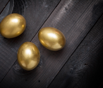 Drei goldene Eier auf dunklem Holzhintergrund