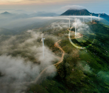 Entlang einer Straße auf einem wolkenverhangenen, grünen Bergrücken stehen Windkrafträger